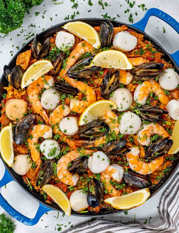 freshly made paella in a paella pan garnished with lemons and parsley.