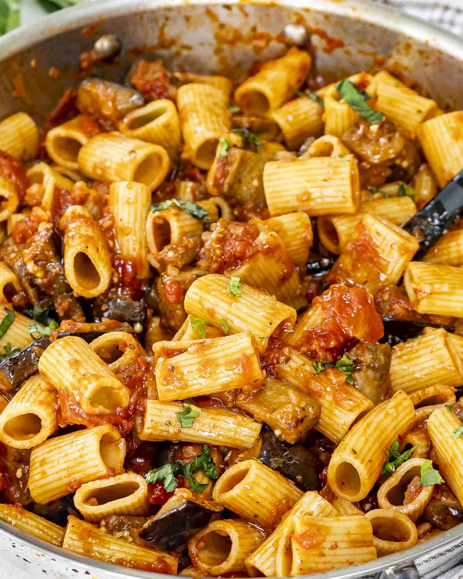 A skillet of Pasta alla Norma featuring rigatoni in a rich tomato sauce with tender eggplant chunks, garnished with fresh basil.