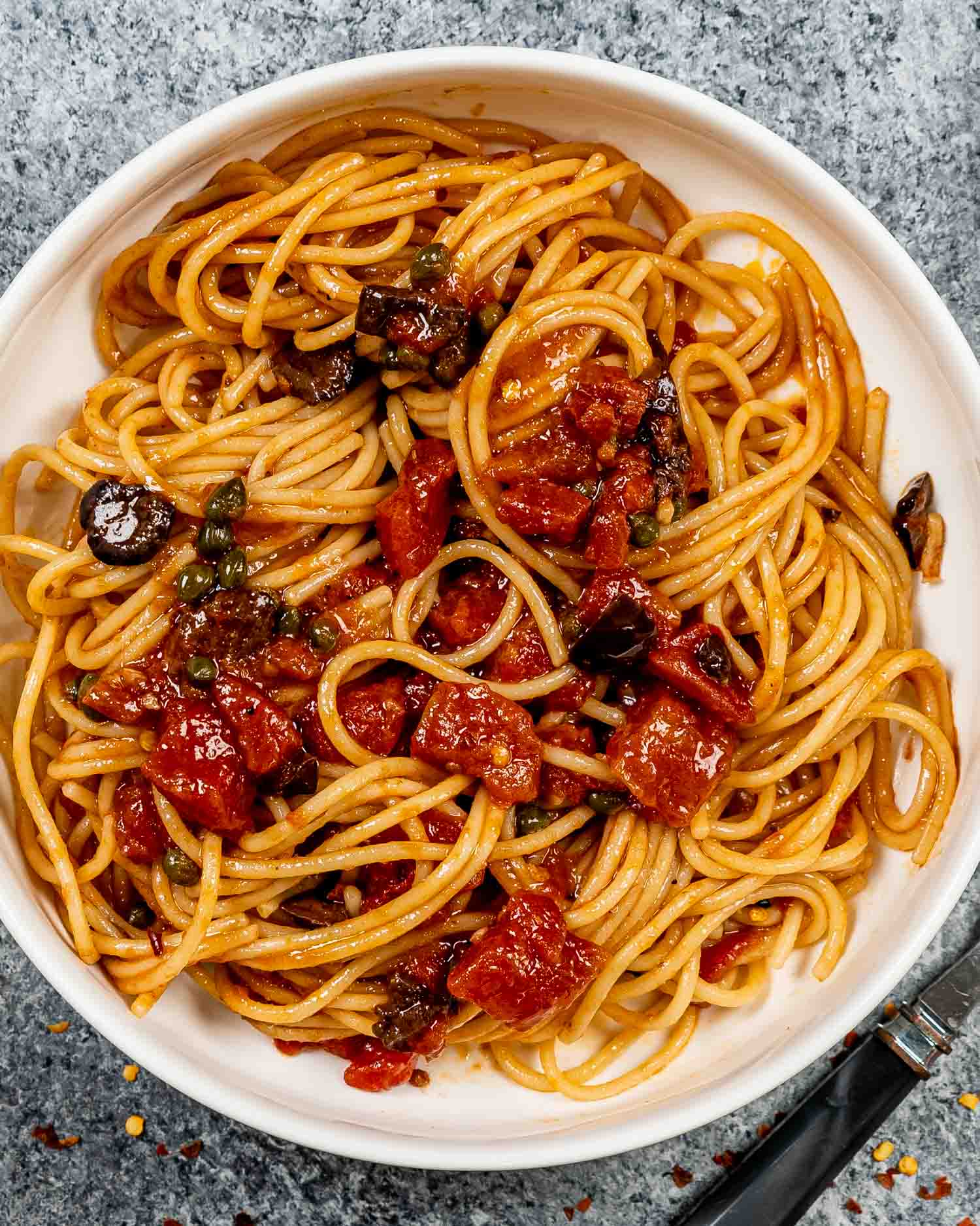 a serving of pasta puttanesca in a white bowl.