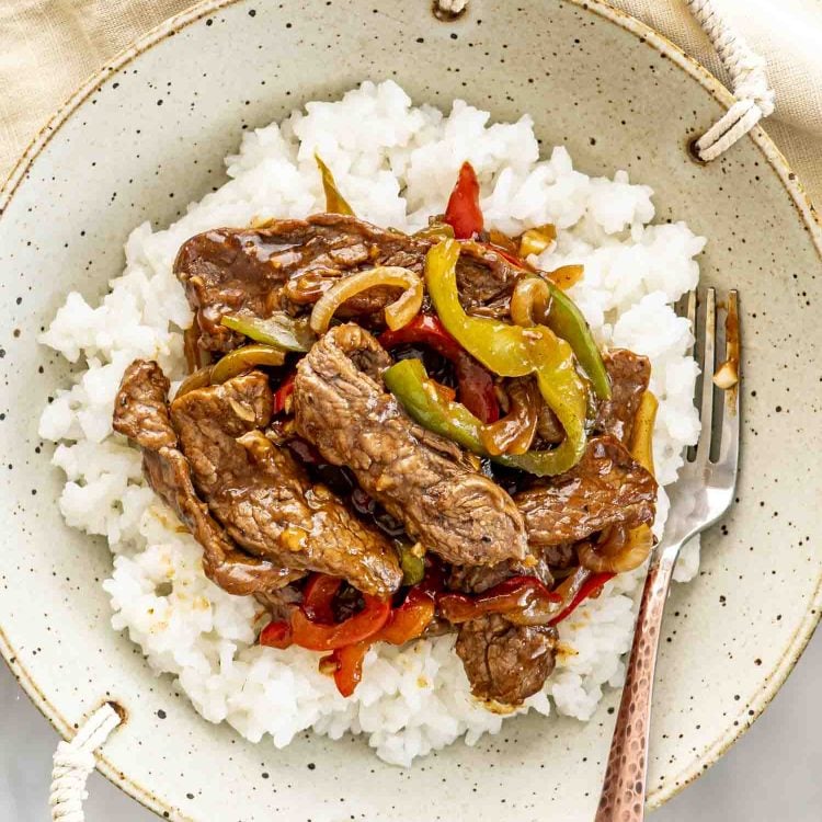 overhead shot of pepper steak over a bed of rice in a bowl.