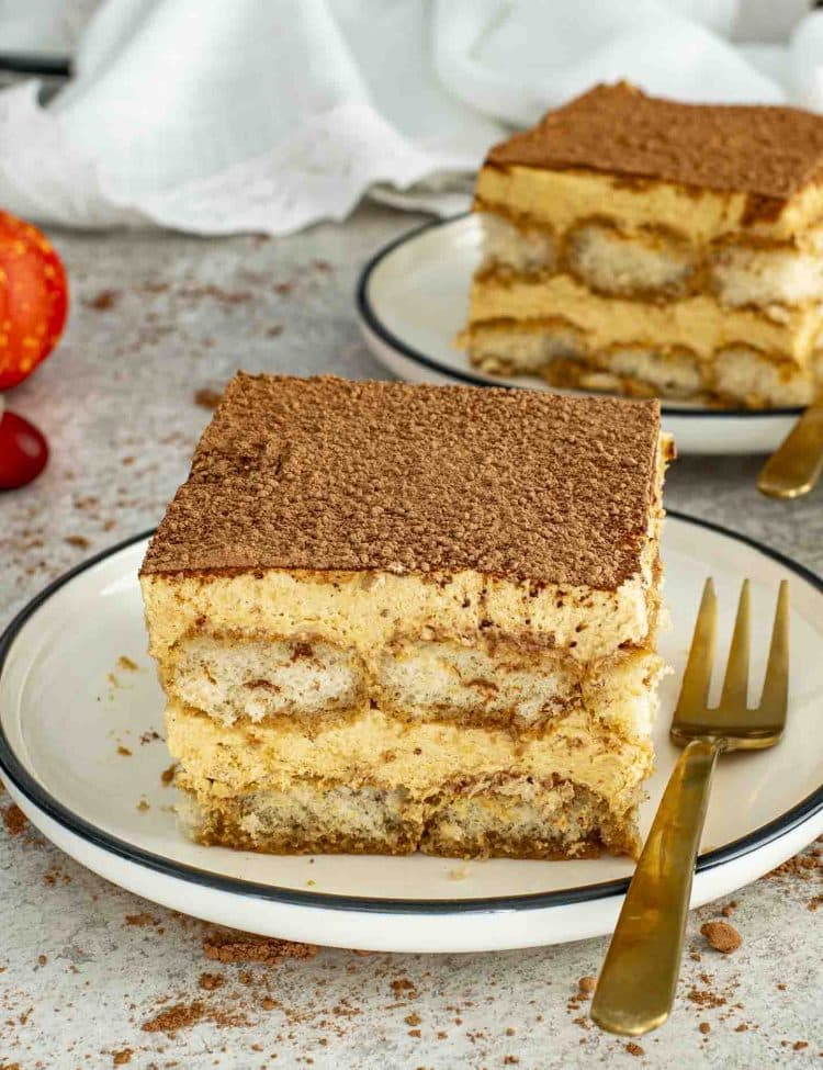 Two square slices of pumpkin tiramisu on plates with golden forks, layered with pumpkin cream and espresso-soaked ladyfingers.