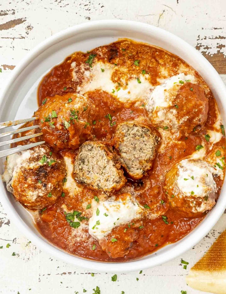 ricotta meatballs with marinara sauce and dollops of ricotta cheese in a white bowl.