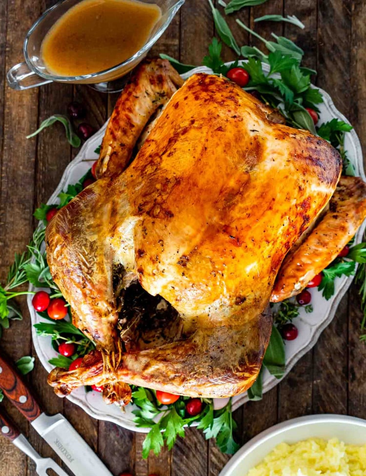 a roast turkey on a turkey platter garnished with herbs and cranberries.