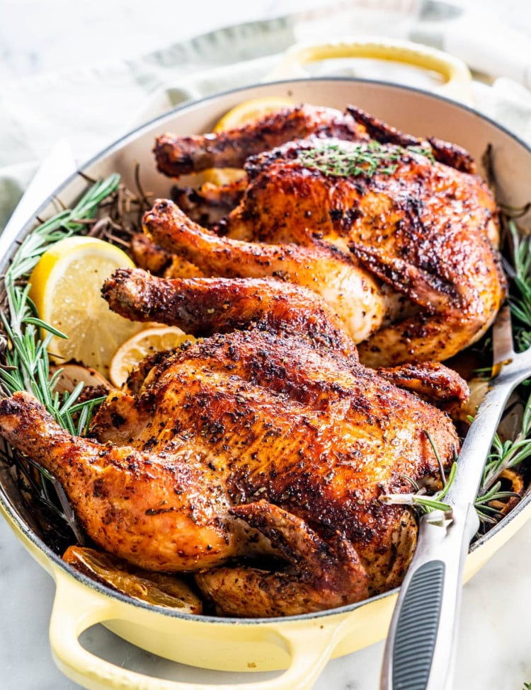 two roasted cornish hens in a roasting pan with sprigs of rosemary and lemon slices
