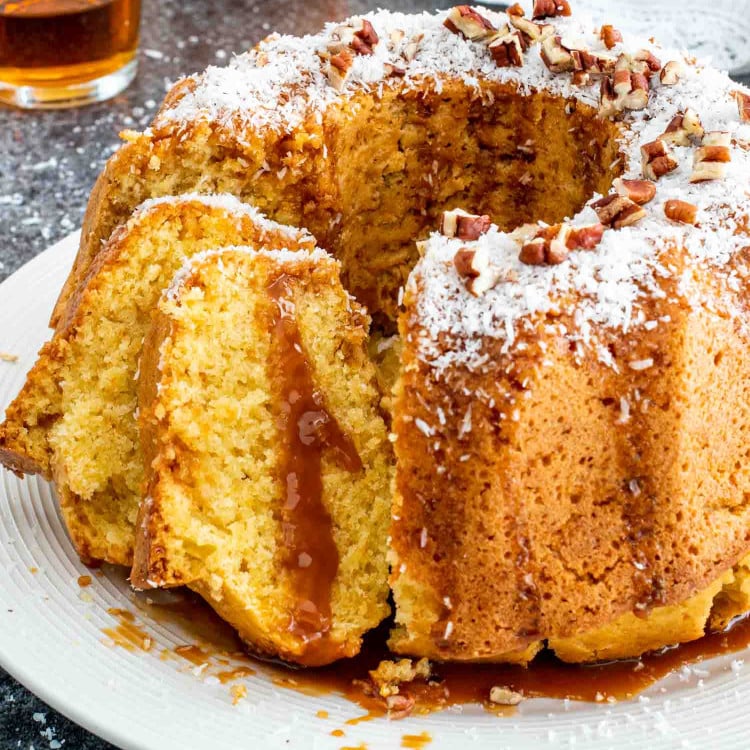 a delicious freshly baked rum cake on a cake plater with a few slices cut out.