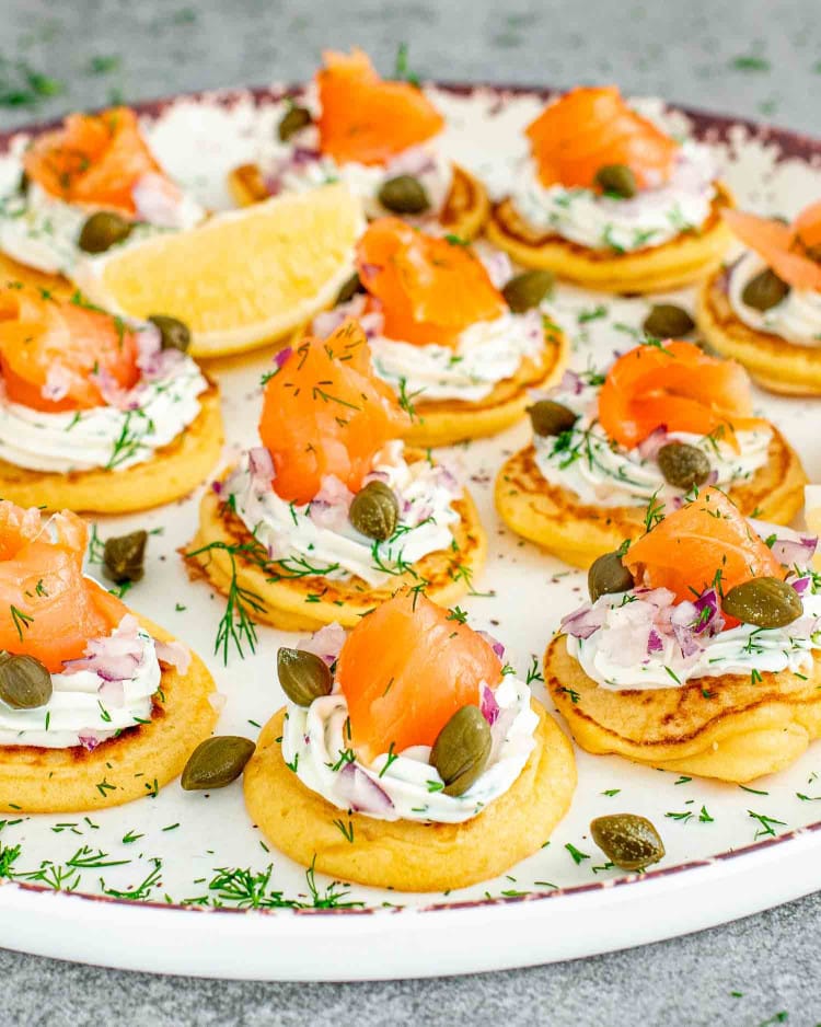 freshly made smoked salmon blinis on a white plate garnished with lemon wedges.