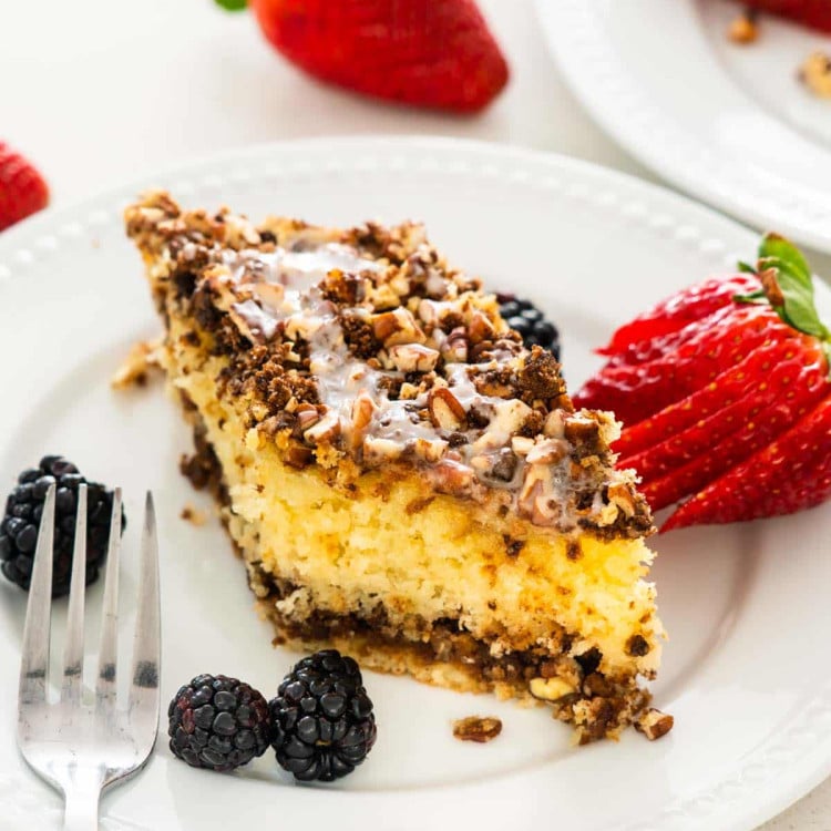 a slice of sour cream coffee cake on a white plate with a strawberry.
