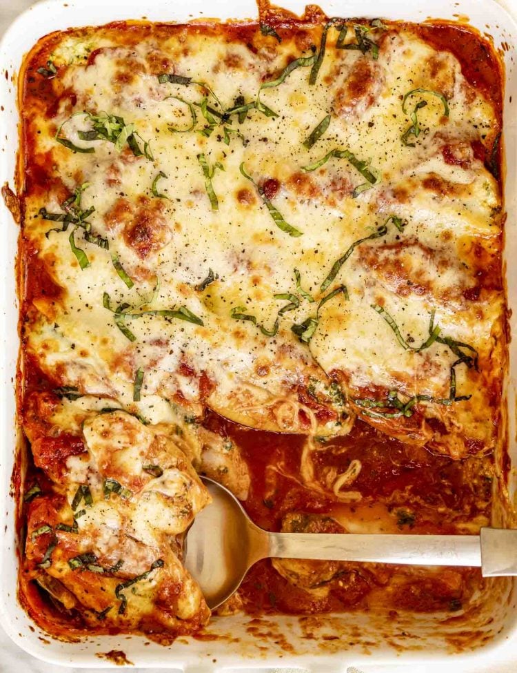 Baking dish full of saucy stuffed shells topped with melted mozzarella and fresh basil, one scoop removed with a spoon.