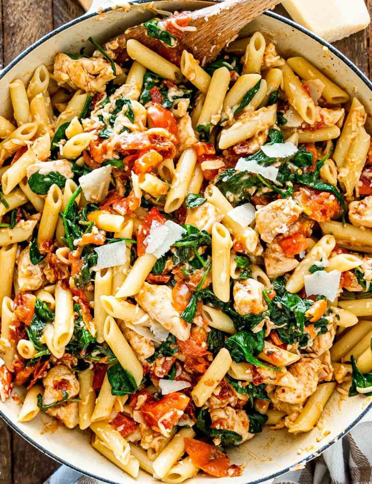 tomato spinach chicken pasta in a white bowl.